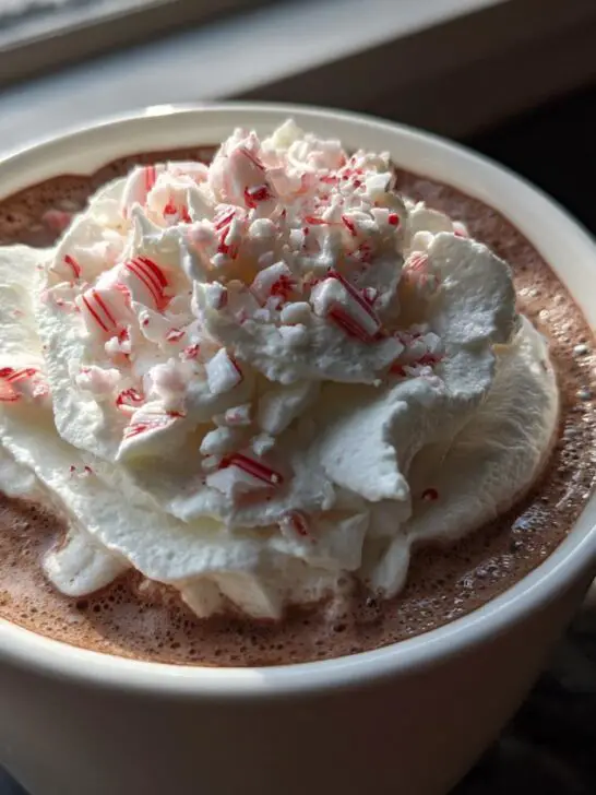 Close-up of a mug filled with Christmas Candy Cane Hot Chocolate, topped with whipped cream and crushed candy canes.
