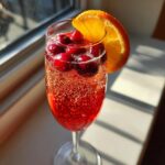 A festive Christmas Cranberry Mimosa in a champagne flute, garnished with fresh cranberries and an orange slice.