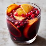 A refreshing glass of Christmas Holiday Sangria with Pomegranate, garnished with orange slices and pomegranate seeds.