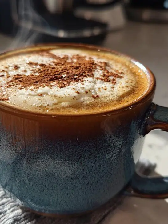 A steaming mug of Christmas Hot Buttered Rum, topped with whipped cream and a dusting of cinnamon.