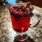A festive glass of Christmas Mulled Cranberry Cider, garnished with cranberries, star anise, and cinnamon sticks.