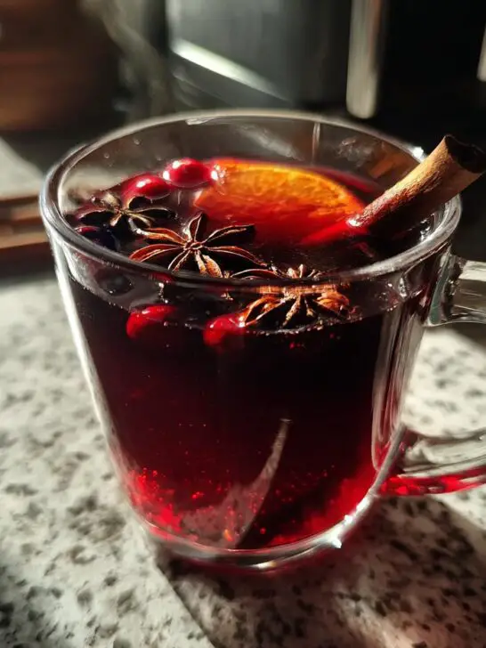A festive mug of Christmas Mulled Cranberry Cider, garnished with cranberries, star anise, an orange slice, and a cinnamon stick.