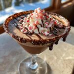 A festive Christmas Peppermint Bark Martini topped with whipped cream, crushed candy canes, and chocolate drizzle.