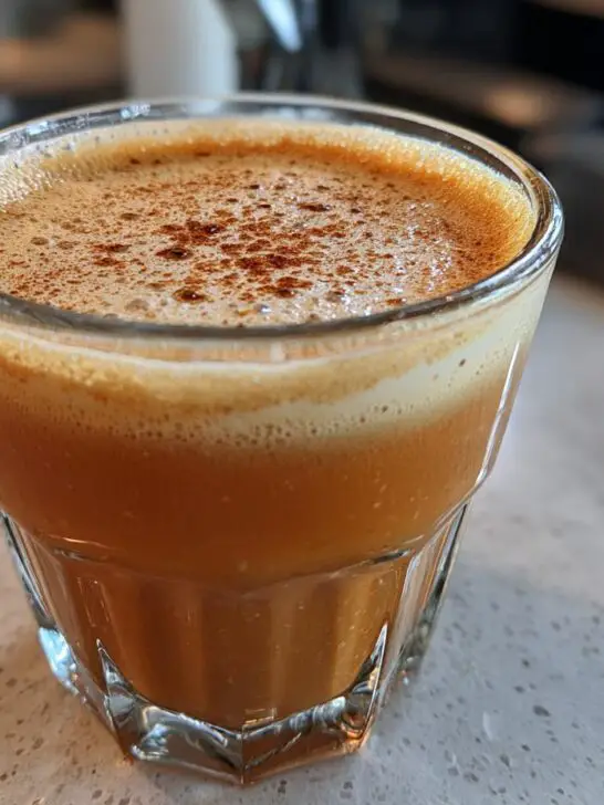 Close-up of a festive Christmas Spiked Chai Eggnog in a glass, topped with foam and a sprinkle of cinnamon.