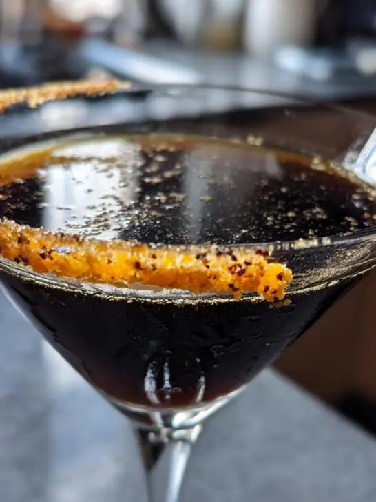 A close-up of a Halloween Black Magic Martini in a martini glass, with a sugar rim and dark liquid.