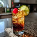 A refreshing Halloween Dark & Spooky Rum and Ginger cocktail with ice, a lime wedge, and a maraschino cherry.