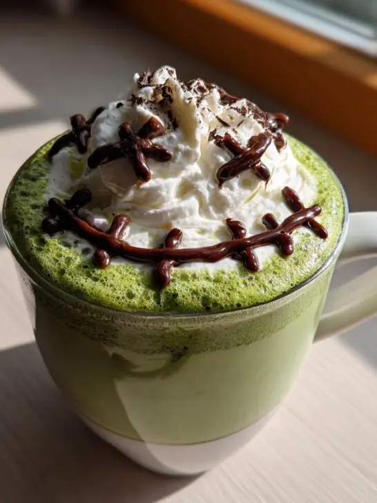 A festive Halloween Frankenstein Matcha Latte topped with whipped cream and chocolate stitches.