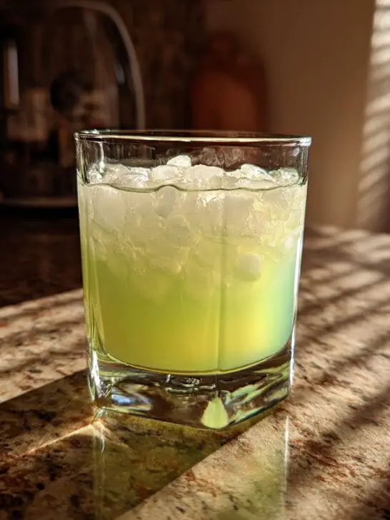 A glass of bright green Halloween Glow-in-the-Dark Lemonade filled with ice.
