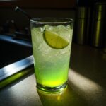 A tall glass filled with Halloween Glow-in-the-Dark Lemonade, ice, and a lime slice.