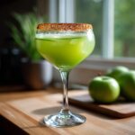 A vibrant green Halloween Poison Apple Margarita in a stemmed glass with a spiced rim, garnished with cucumber slices.