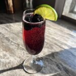 A refreshing New Year’s Eve Blackberry Sparkler cocktail in a champagne flute, garnished with blackberries and a lime wedge.