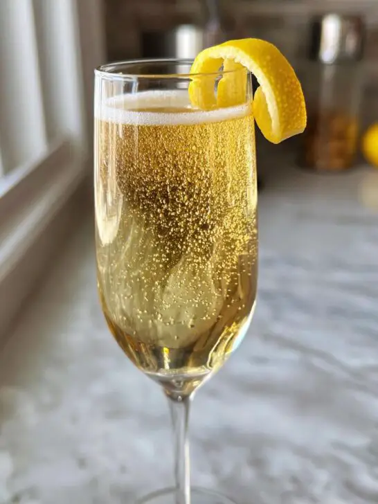 A bubbly New Year’s Eve Elderflower Champagne Fizz cocktail in a flute glass, garnished with a lemon twist.