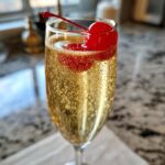 A festive New Year’s Eve Gold Rush Champagne cocktail garnished with a bright red cherry.