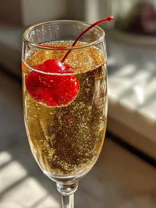A festive New Year’s Eve Gold Rush Champagne cocktail garnished with a maraschino cherry and edible glitter.