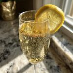 Close-up of a New Year’s Eve Golden Glitter Champagne Cocktail in a flute glass with a lemon slice garnish.