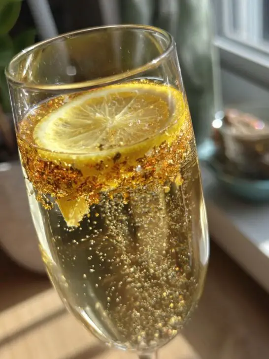 A festive New Year’s Eve Golden Glitter Champagne Cocktail with a lemon slice and edible glitter.