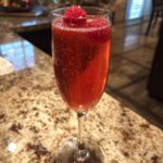 A festive New Year’s Eve Midnight Kiss Cocktail in a champagne flute, garnished with fresh raspberries.