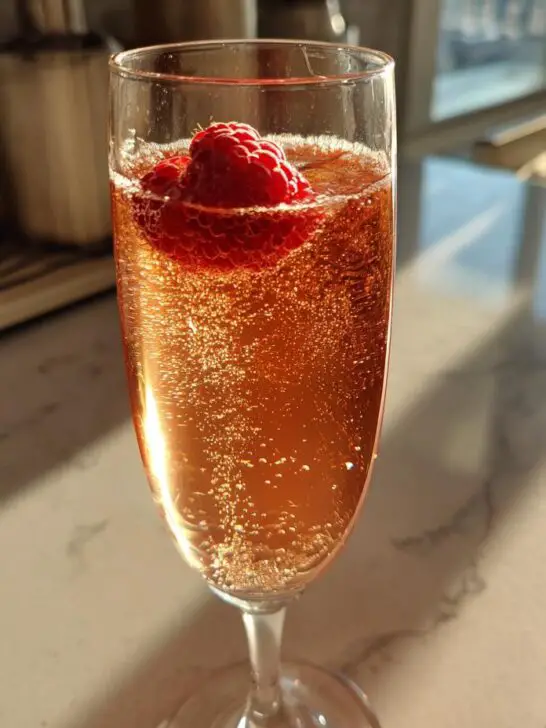 A festive New Year’s Eve Midnight Kiss Cocktail in a champagne flute, garnished with a fresh raspberry.