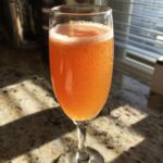 A close-up of a New Year’s Eve Peach Bellini in a champagne flute, with bubbles and a golden-orange hue.