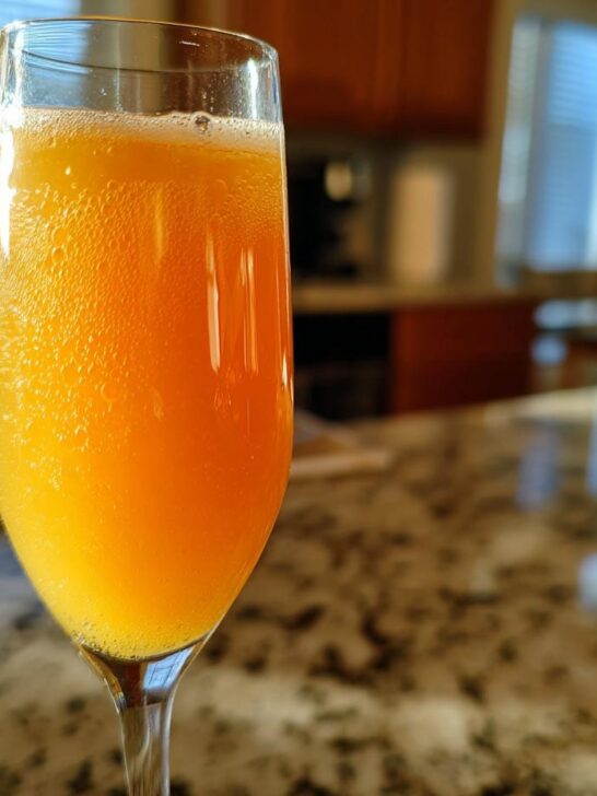 A refreshing New Year's Eve Peach Bellini cocktail in a champagne flute, with bubbles rising.