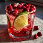 A refreshing New Year's Eve Sparkling Cranberry Ginger Mocktail garnished with fresh cranberries and a lime wedge.