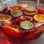 A close-up of a festive New Year’s Eve Sparkling Pomegranate Punch in a glass bowl, garnished with pomegranate seeds, orange slices, and lime slices.