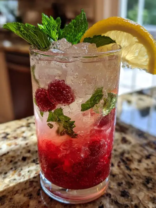 A refreshing New Year's Eve Sparkling Raspberry Lemonade with fresh raspberries, mint, and a lemon slice.