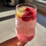 A tall glass filled with Sparkling Raspberry Lemonade, garnished with fresh raspberries and lemon slices.