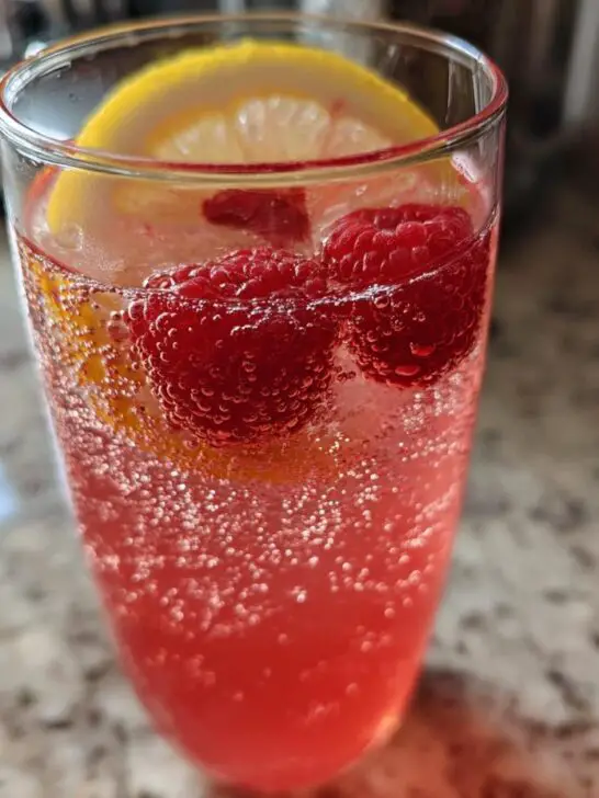 A refreshing glass of Sparkling Raspberry Lemonade with fresh raspberries and lemon slices, full of bubbles.