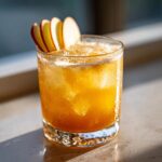 A refreshing Thanksgiving Apple Butter Whiskey Sour cocktail with apple slices and ice.