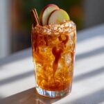 A refreshing Thanksgiving Caramel Apple Mocktail garnished with apple slices, cinnamon sticks, and a drizzle of caramel.