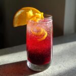 A refreshing Thanksgiving Cranberry Orange Sparkler cocktail in a tall glass, garnished with an orange slice and zest.