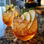 Two glasses of Thanksgiving Ginger Pear Spritz cocktail with ice, pear slices, and rosemary sprigs.