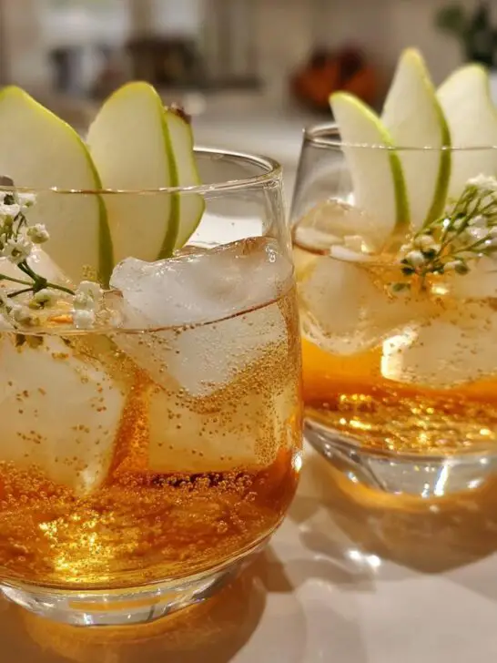 Two glasses of Thanksgiving Ginger Pear Spritz cocktail with ice, pear slices, and delicate white flowers.