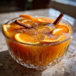 A crystal bowl filled with Thanksgiving Pumpkin Cider Punch, garnished with orange slices and cinnamon sticks.