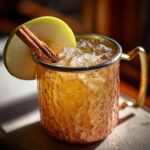 A refreshing Thanksgiving Spiced Pear Mule cocktail in a hammered copper mug, garnished with a green apple slice and cinnamon stick.