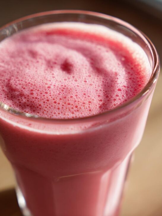 Close-up of a frothy Valentine’s Day Pink Velvet Smoothie in a clear glass, with a swirl on top.