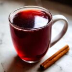 A steaming mug of Valentine’s Day Red Hot Cinnamon Cider with a cinnamon stick on the side.