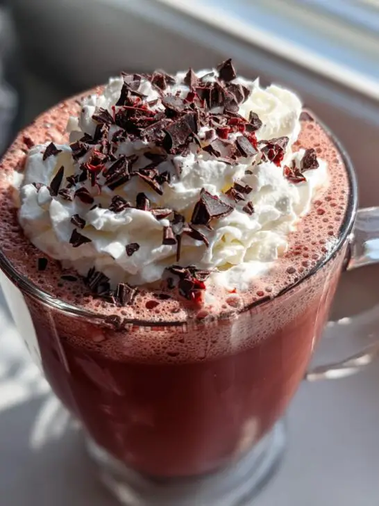 A close-up of a Valentine's Day Red Velvet Hot Chocolate topped with whipped cream and chocolate shavings.