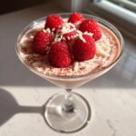 A close-up of a Valentine’s Day White Chocolate Raspberry Martini topped with fresh raspberries and white chocolate shavings.