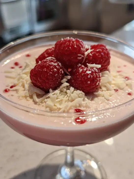A festive Valentine’s Day White Chocolate Raspberry Martini garnished with fresh raspberries and white chocolate shavings.