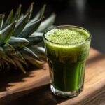 A glass of vibrant green Apple Carrot Ginger Energy Juice, with a pineapple in the background.