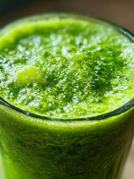 Close-up of a glass filled with vibrant green Apple Carrot Ginger Energy Juice, topped with foam.