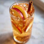 A tall glass filled with a sparkling Apple Cinnamon Mocktail, garnished with apple slices and a cinnamon stick.