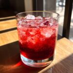 A close-up of a vibrant red Beet & Berry Vodka Refresher cocktail filled with ice and berries.