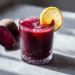 A refreshing beetroot energy shot with ice and a lemon slice, next to fresh beetroots.