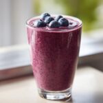 A refreshing glass of Blueberry Maca Power Smoothie topped with fresh blueberries.