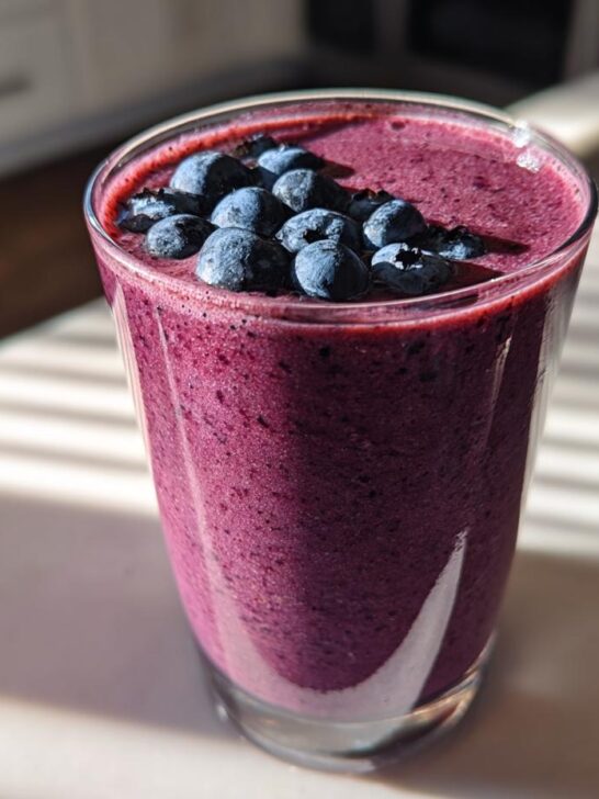 A glass of vibrant purple Blueberry Maca Power Smoothie topped with fresh blueberries.