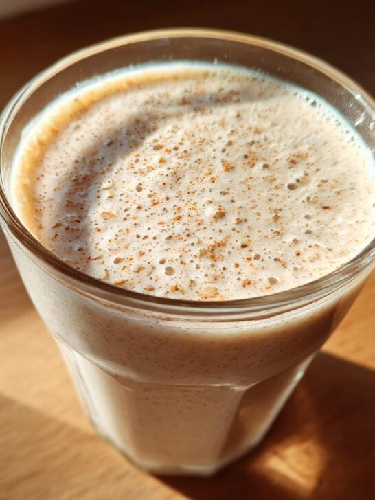 Close-up of a frothy Blueberry Maca Power Smoothie in a glass, sprinkled with cinnamon.