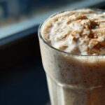 Close-up of a Blueberry Maca Power Smoothie in a glass, topped with oats and cinnamon.